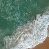 Luchtbeeld van golven en schuim langs een zandstrand