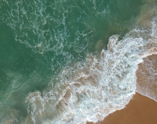 Luchtbeeld van golven en schuim langs een zandstrand