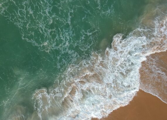 Luchtbeeld van golven en schuim langs een zandstrand